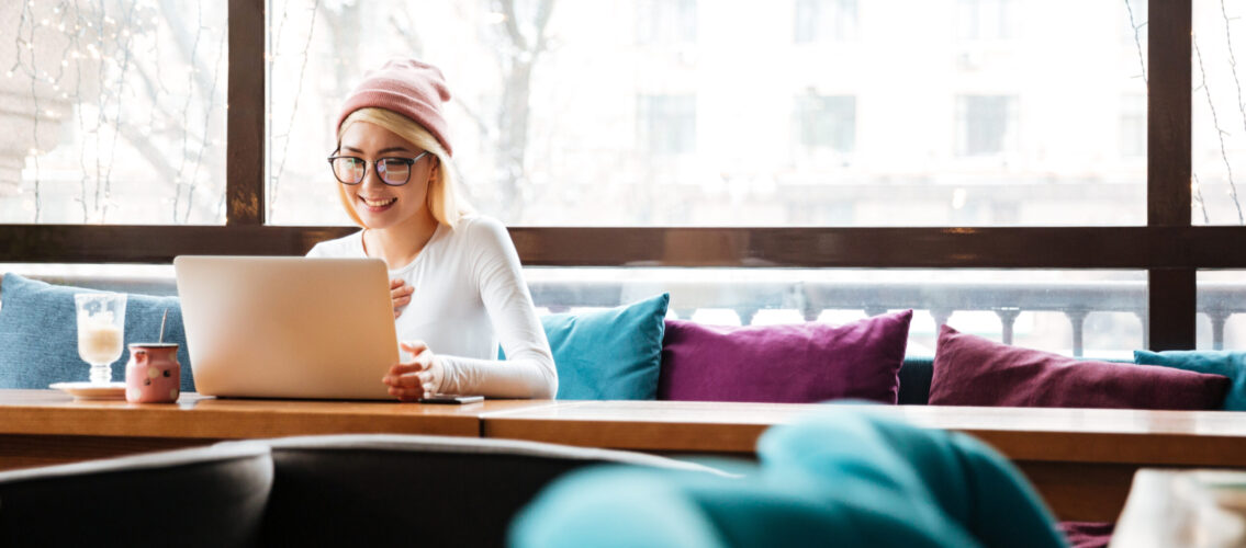 Cheerful young woman sitting and using laptop in cafe